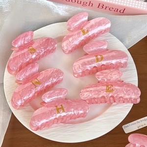 Set de pinzas para el cabello rosa mármol con letras doradas en un plato blanco