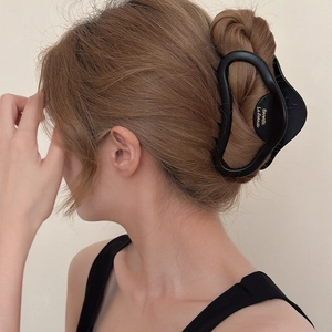 Gros plan d'une grande pince à cheveux noire mate fixant un chignon volumineux