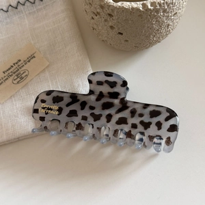 Detailed view of large leopard print hair claw clip with golden brand logo on a soft background