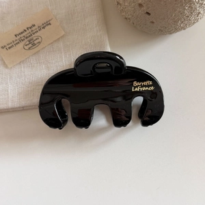 Detail of glossy black three-prong hair claw clip with golden lettering on fabric texture