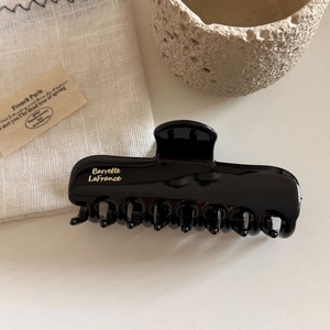 Close-up of a large glossy black hair claw clip with golden French lettering detail