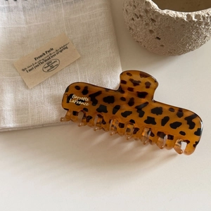 Detail showing high-gloss leopard print hair claw clip on soft beige linen fabric
