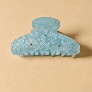 Détail de la pince à cheveux en acrylique bleu clair avec texture marbrée et strass