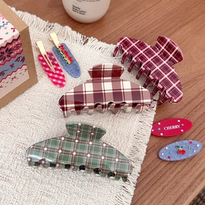 Detail of plaid shark hair clips and cherry hairpins on a wooden desk with a cream mat