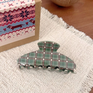 Detail of a large dark green plaid hair claw clip on soft textured fabric background