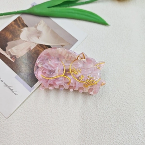 Détail de la pince à cheveux en acétate marbré rose avec motif de chat doré gravé