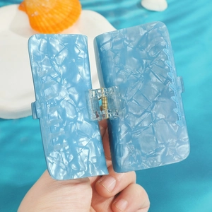 Détail de la pince à cheveux carrée bleu clair avec texture givrée sur fond aquatique