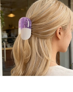 Detail of purple and white pill-shaped hair claw clip styled on blonde wavy hair