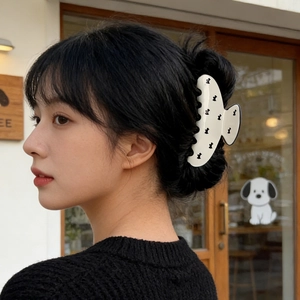 Close-up of a white acetate hair claw with black dog patterns on a sleek updo hairstyle