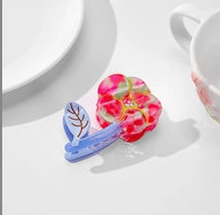 Détail d'une pince à cheveux en acétate avec motif floral rose et feuilles bleues