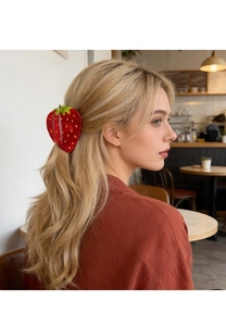 Vue détaillée d'une pince à cheveux fraise rouge portée par un mannequin blond au café