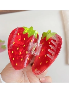 Détail d'une pince à cheveux en forme de fraise rouge avec des feuilles vertes