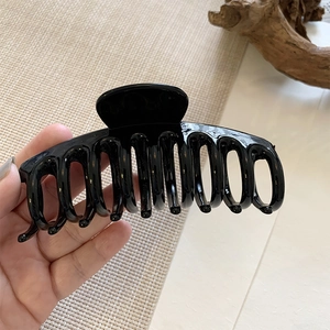 Detail of glossy black large hair claw clip held in hand for thick hair styling