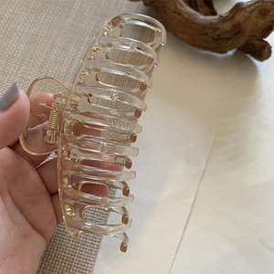 Detail of large amber resin hair claw clip with golden spring held in hand for styling