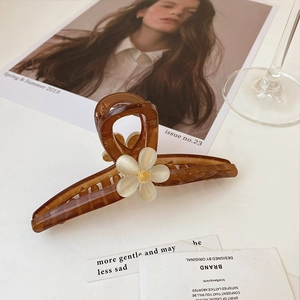 Détail de la pince à cheveux écaille ambrée avec fleur blanche sur fond de magazine