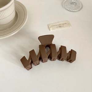 Détail de la grande pince à cheveux géométrique marron mat sur fond minimaliste