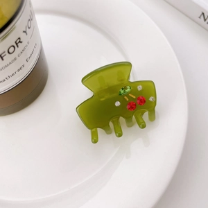 Green translucent acetate hair claw clip with crystal cherry patterns on a white tray