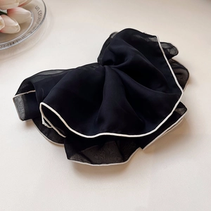 Dettaglio di un grande elastico in tulle nero con bordo bianco su sfondo crema minimale