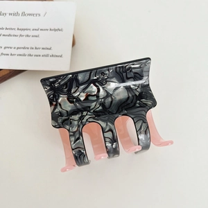 Detail of square acetate hair claw clip featuring black marble pattern and pink teeth