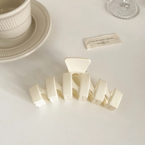Grosse pince à cheveux beige mat sur un bureau minimaliste avec tasse de café