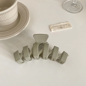 Pince à cheveux géométrique vert olive mat à côté d'une tasse à café et carte