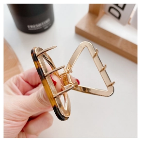 Detailed view of a golden geometric hair claw with tortoiseshell resin inlays and springs