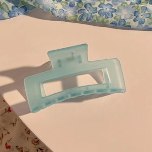 Nahaufnahme einer matt hellblauen quadratischen Haarklammer mit Blumendetail