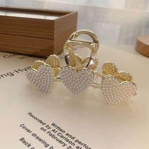 Detailaufnahme der goldenen Herz-Haarklammer mit Perlenbesatz und eleganter Metallfeder