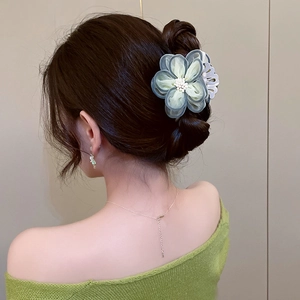 Close-up of translucent camellia hair claw clip with pearls on a green knit sweater