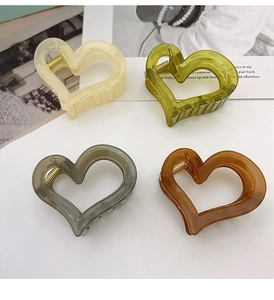 Detail view of heart-shaped hair claw clips in beige, green, amber, and grey resin