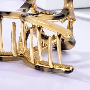 Macro detail of tortoiseshell resin and gold metal hair claw clip with non-slip teeth