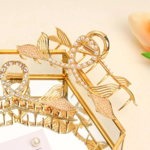 Close-up of golden fishtail hair claw clip with pearls and rhinestones on beige surface