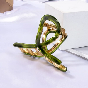 Close-up of deep green acetate hair claw clip with golden metal teeth on white silk