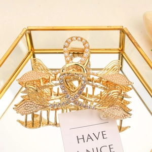 Detailed close-up of golden metal fishtail hair claw clip with pearls and rhinestones
