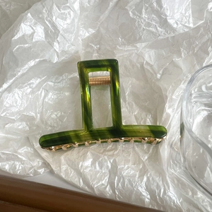 Macro view of dark green marble acetate hair claw clip with golden metal teeth detail