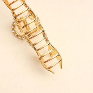 Detail of golden fish tail hair claw clip featuring elegant rhinestones and metal spring