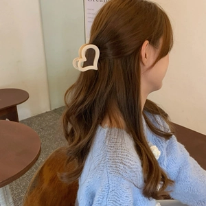 Elegante pinza per capelli a forma di cuore color crema opaco su capelli castani in un caffè
