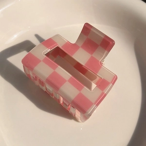 Detailed view of pink and white checkered hair claw clip on a white ceramic plate