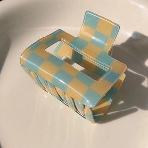 Close-up detail of blue and beige checkerboard hair claw clip in a white ceramic bowl