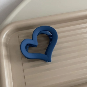 Dettaglio della pinza per capelli a cuore blu opaco su un vassoio beige strutturato