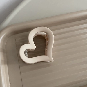 Dettaglio della molletta per capelli opaca a forma di cuore beige su vassoio