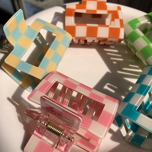 Colorful checkered acrylic hair claws in pink, orange, and blue on a white display plate