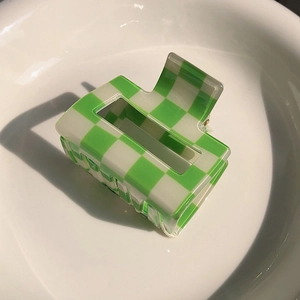 Detail view of green and white checkered hair claw clip on a white ceramic plate