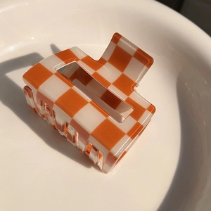 Detail showing orange and white checkerboard hair claw clip with glossy acrylic finish
