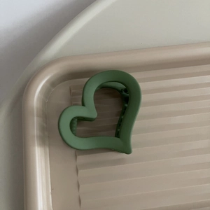 Dettaglio macro della molletta per capelli a cuore in verde opaco sul vassoio
