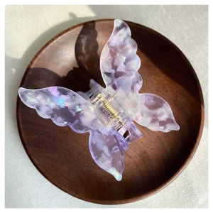 Detailed close-up of butterfly hair claw clip with purple marble texture on wooden tray