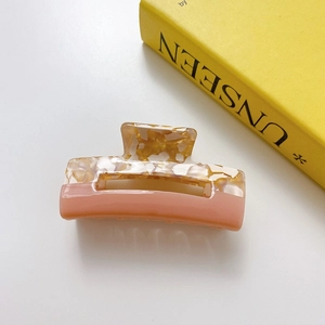 Detail of a square cutout hair claw clip with marble yellow and dusty pink color block