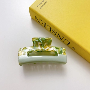 Detail view of acetate square hair claw clip with green amber texture and metal spring