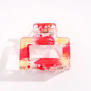 Détail d'une grande pince à cheveux carrée transparente avec éclaboussures rouge et or