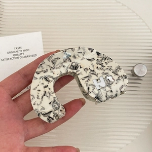 Macro shot of acetic acid hair claw clip with black and white marble pattern and H charm